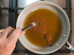 Cinnamon being added to honey syrup in a pan.
