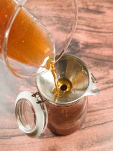 Pouring cinnamon honey syrup through a funnel into a jar.