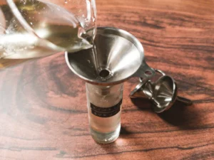 Pouring classic simple syrup through a funnel into a bottle.
