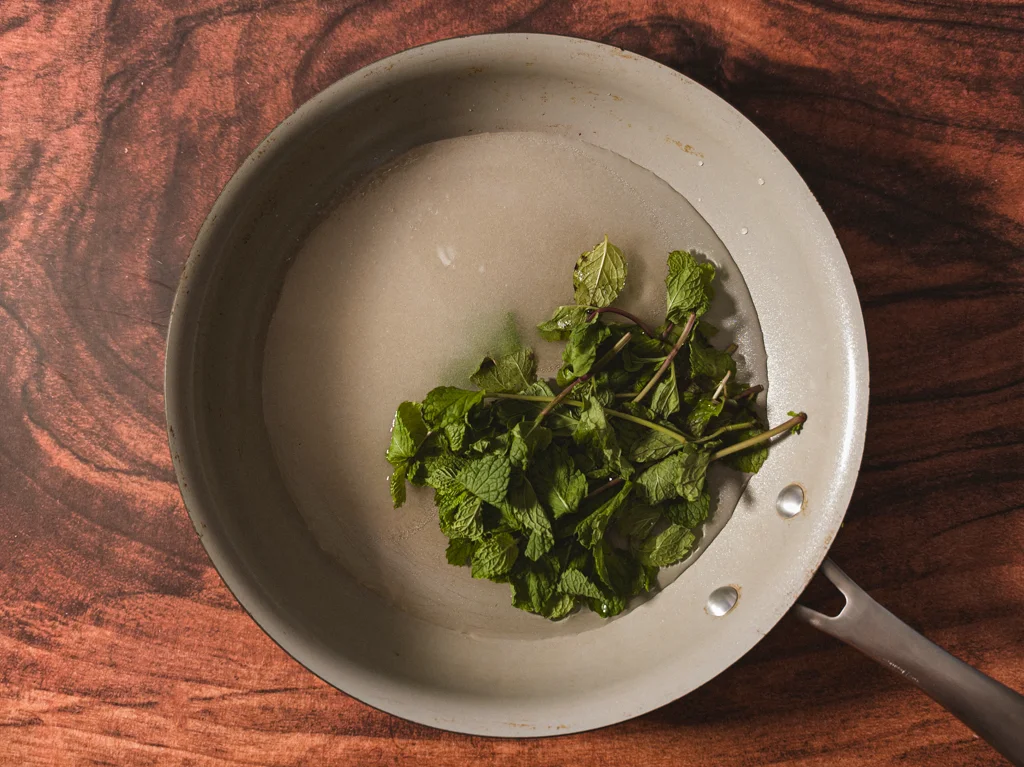 Medium saucepan filled with water, sugar, and mint sprigs.