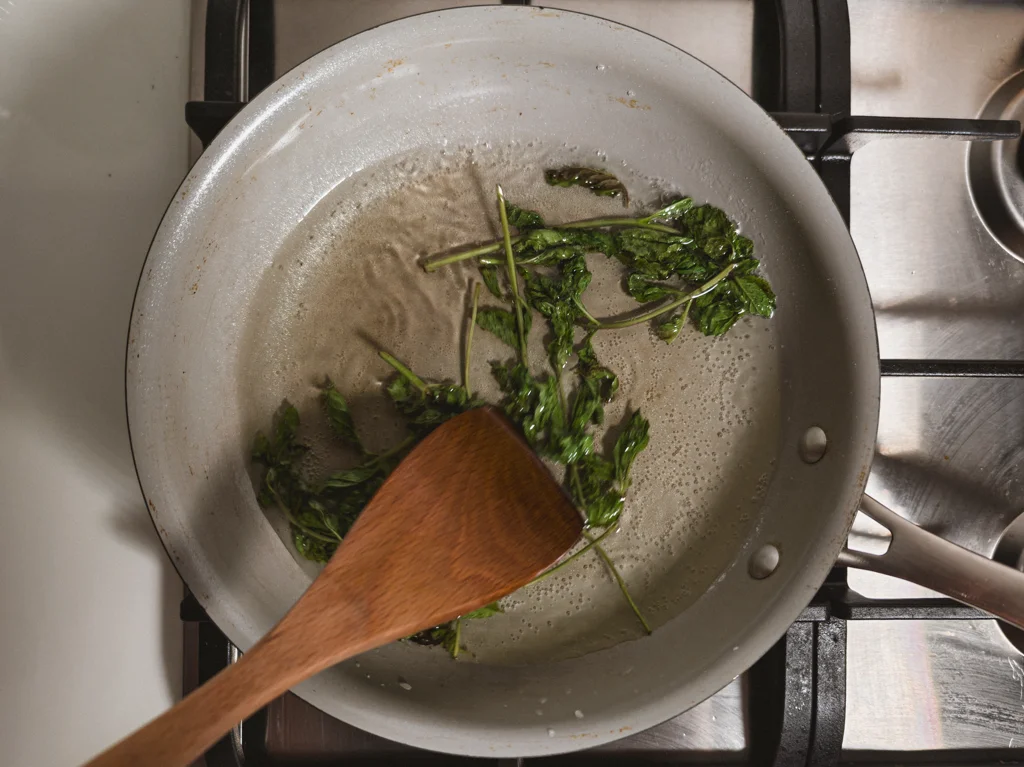 Wooden spoon stirring sugar water and mint sprigs in a medium saucepan.