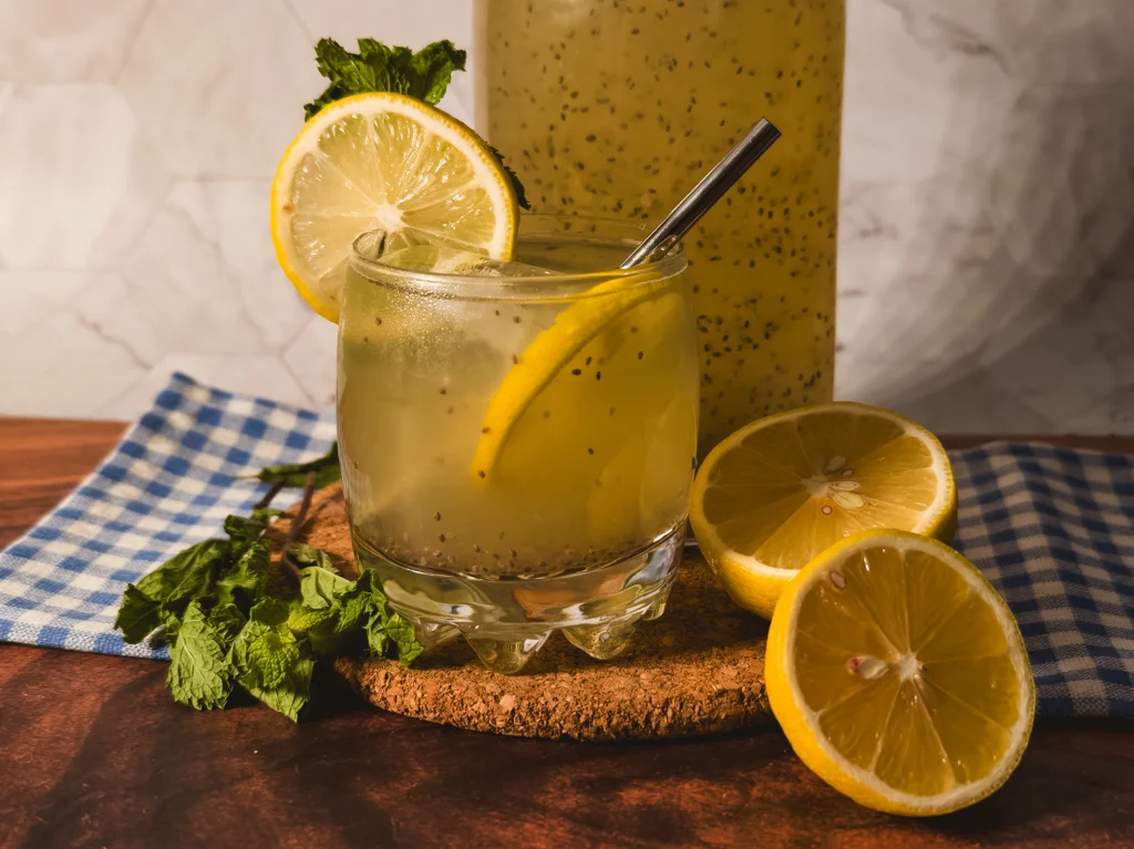 A cocktail glass filled with coconut chia lemonade with mint simple syrup with a metal straw, lemon wheel slice, and mint sprig inside. Garnished with mint sprigs and lemons.